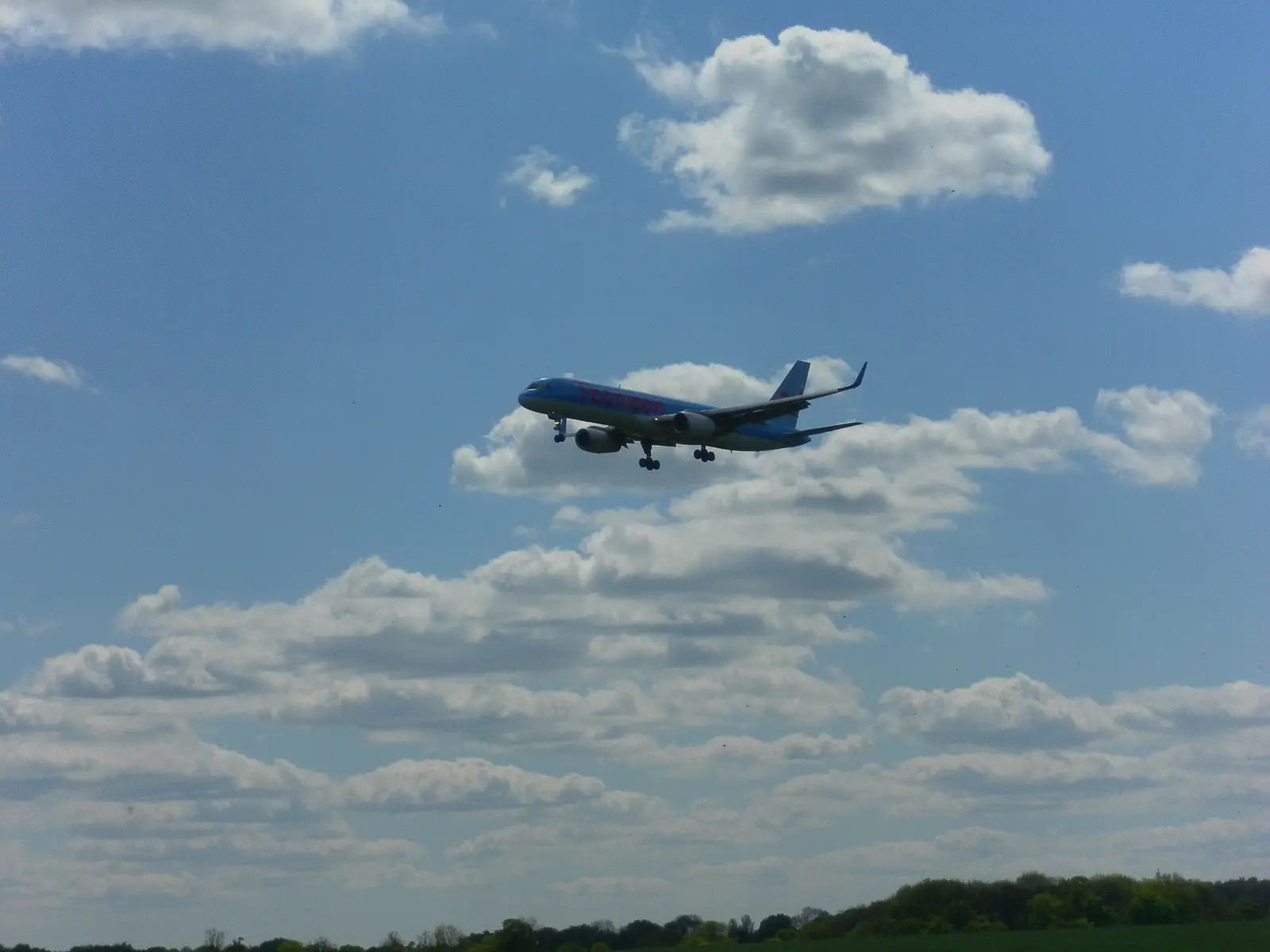 An airliner on final approach under a sky of scattered cloud