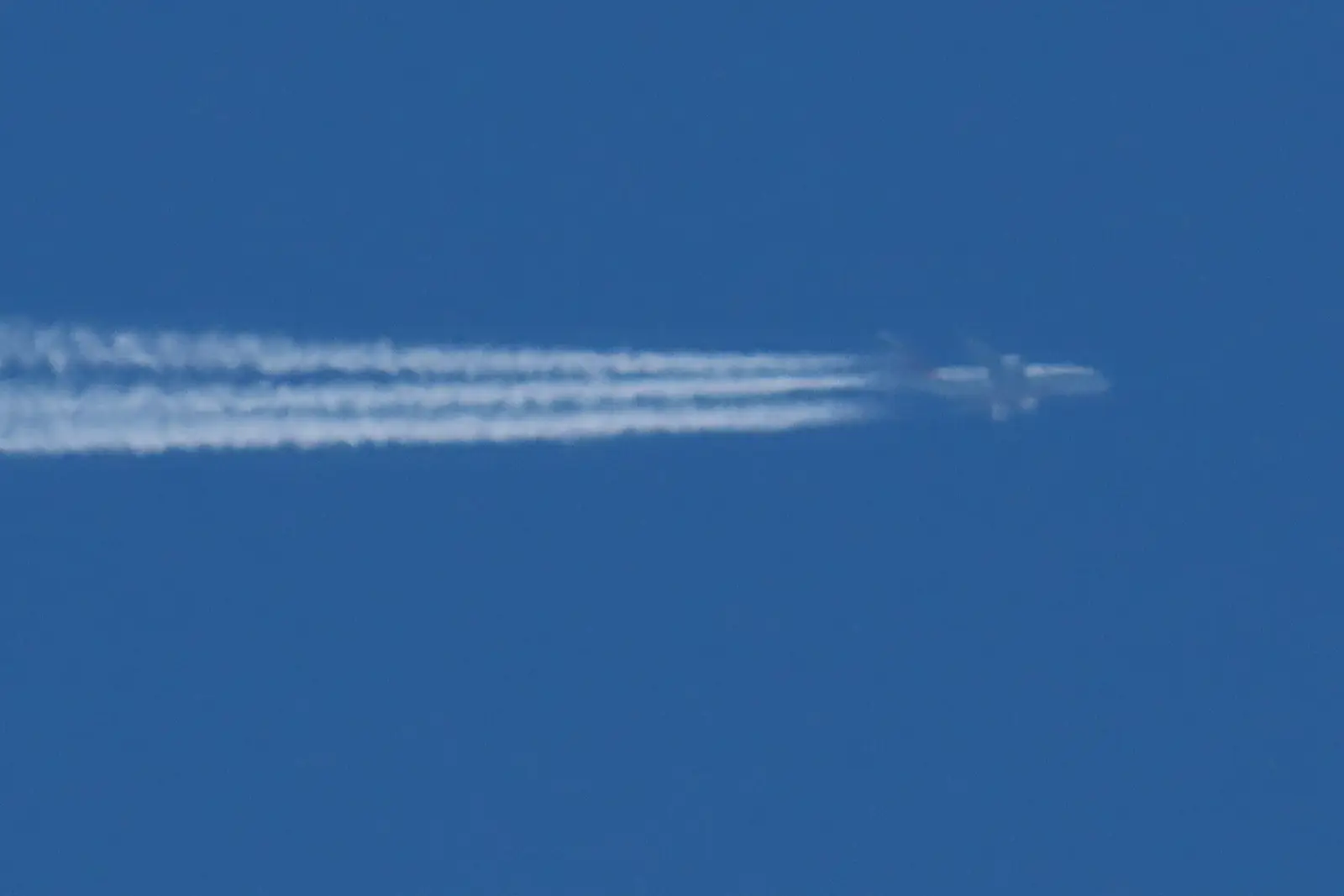An airliner at cruising altitude trailing a long contrail across a blue sky