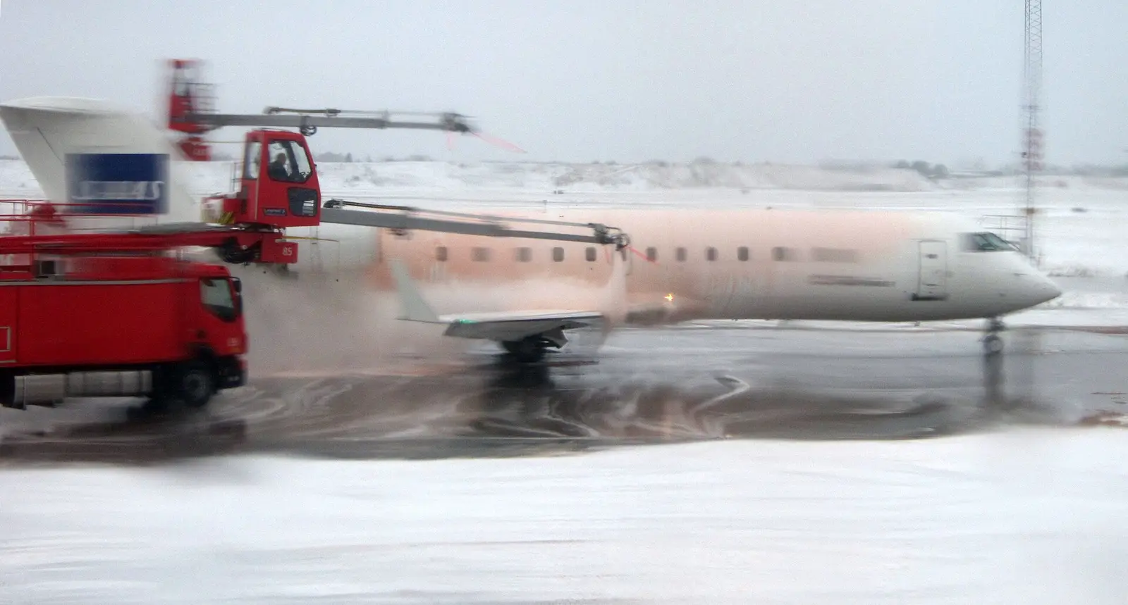 A de-icing truck spraying an airliner in falling snow