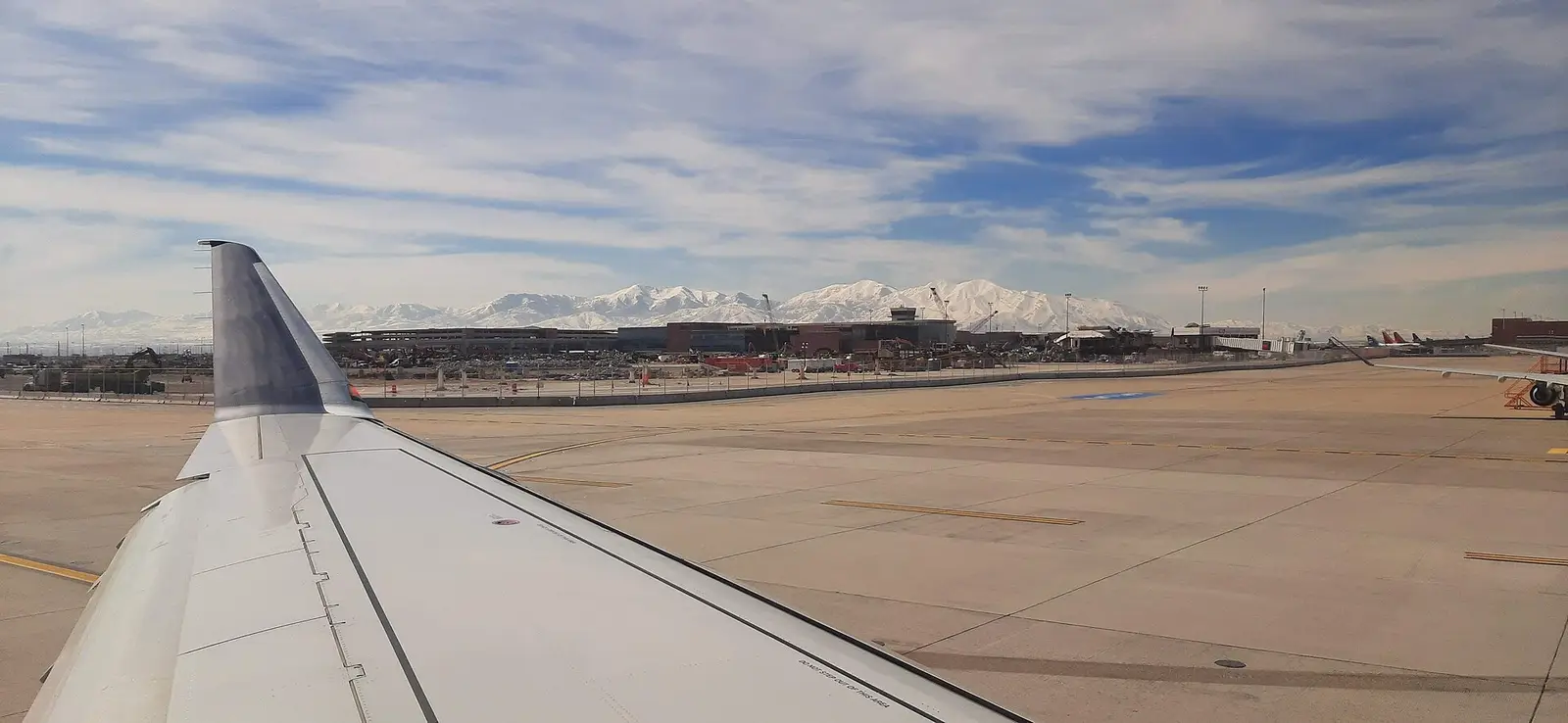 Aircraft wing over the apron at Salt Lake City International Airport with snow-covered mountains behind